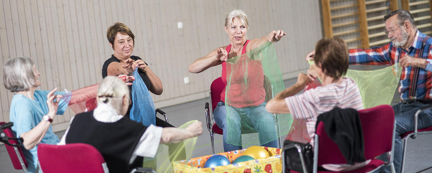 Ältere Menschen im Stuhlkreis bewegen sich mit Tüchern