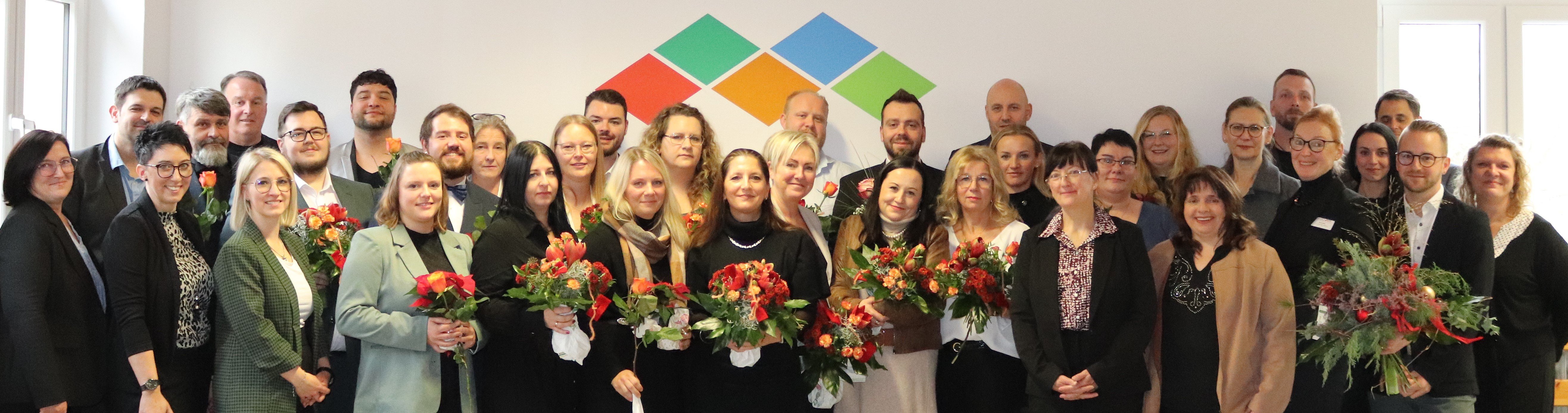 Eine große Gruppe stellt sich zum Gruppenbild auf. Zu sehen sind die Absolventen des Stationsleiterkurses, sie halten Blumen in den Händen, und deren Vorgesetzte.