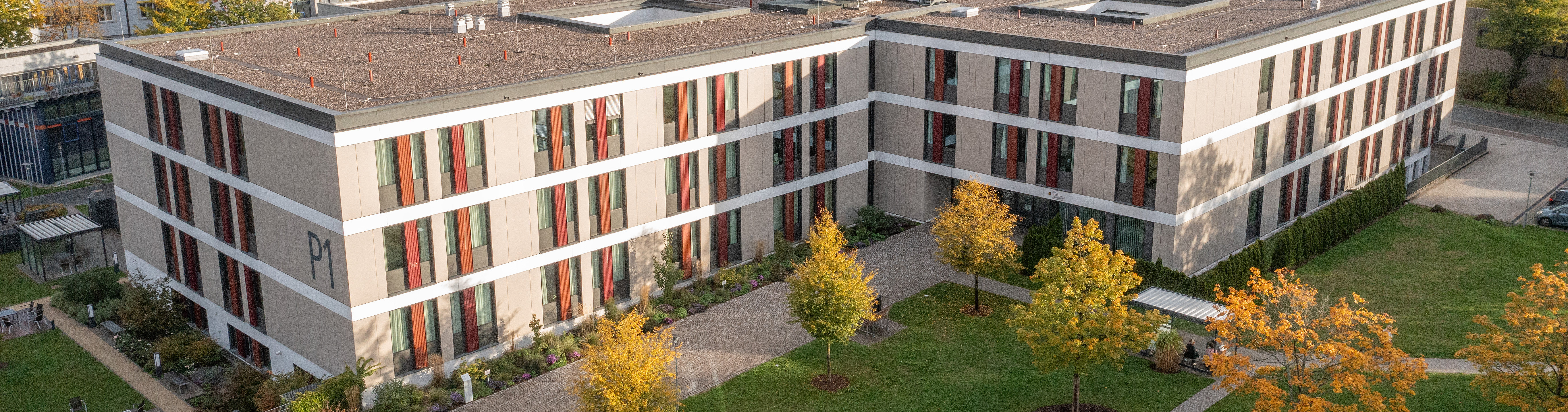 Das Bild zeigt eine Luftaufnahme eines Klinikgebäudes auf dem Gelände des Bezirkskrankenhauses Bayreuth. Es ist sonniges Herbstwetter