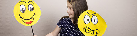  Mädchen hält Emojis mit lachendem und traurigem Gesicht hoch.